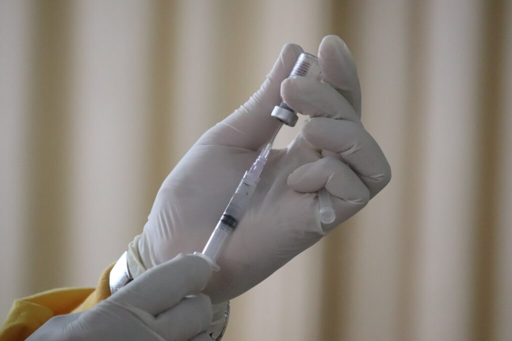 Una mano con un guante blanco afirmando un frasco que contiene una vacuna.